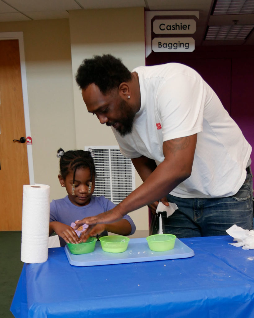 A parent volunteer helps a small girl with her bowl of squishy, gooshey, mushy stuff.
