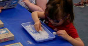 A small girl plays with a tray of Insta Snow.