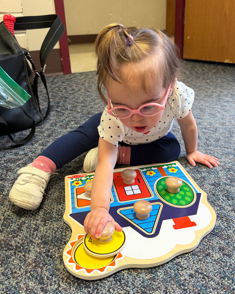 Elise is sitting on the floor and putting puzzle pieces on the board.