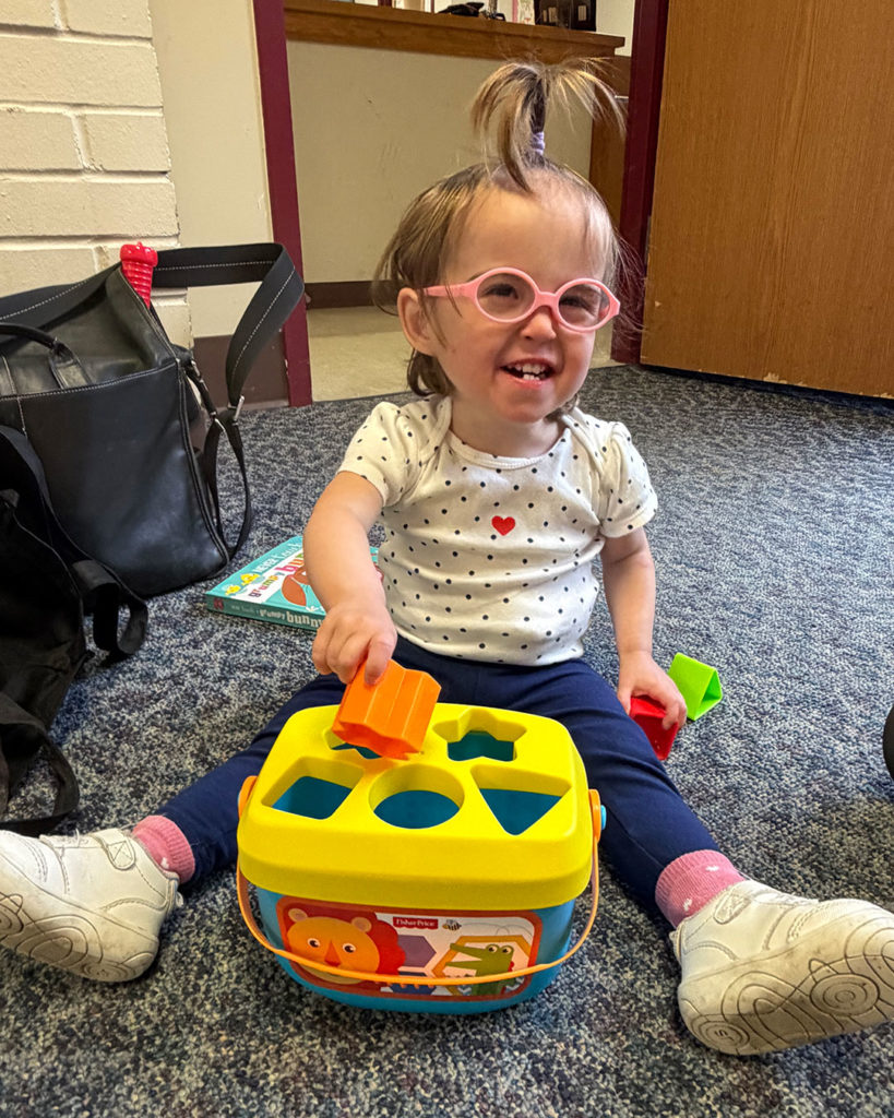 Elise is sitting on the floor and playing with a shape sorter.