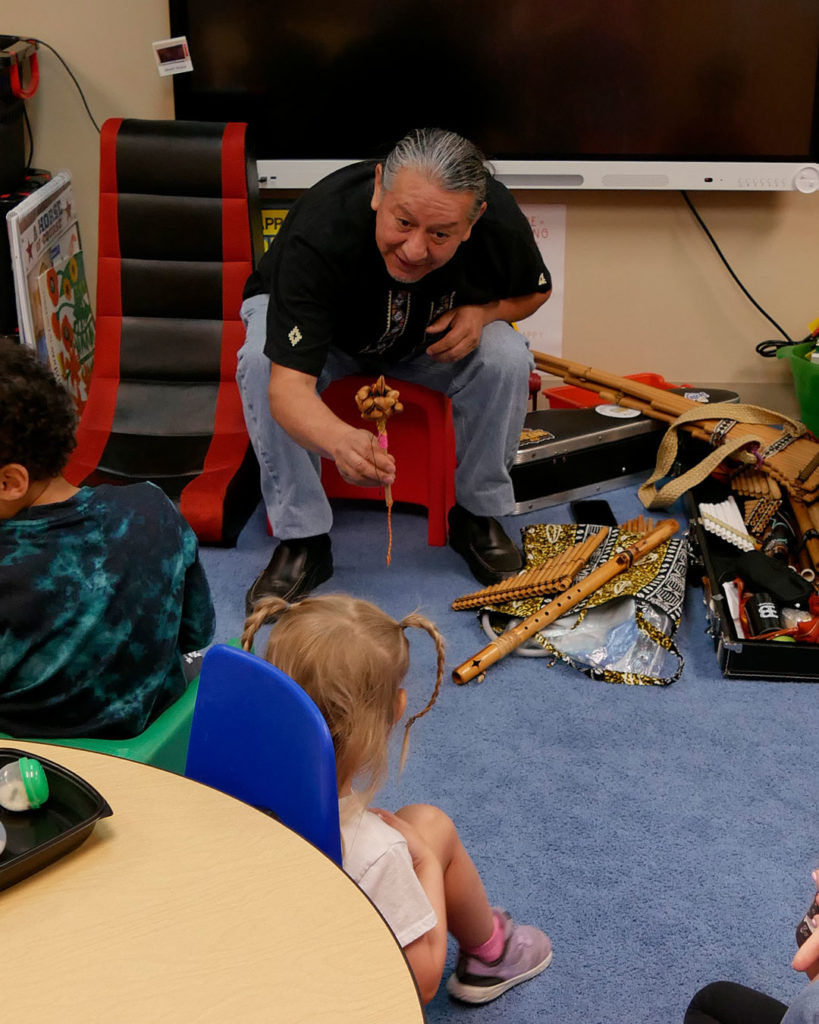 Fernando from Louisville Folk School hands a shaker to a student.