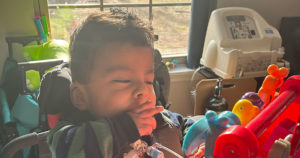 Angelito sits in a chair and plays with an interactive toy.
