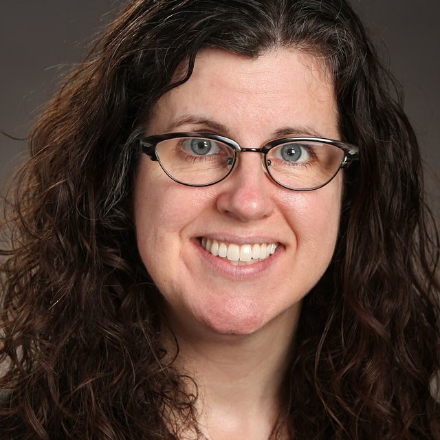 Woman with dark brown hair and glasses smiling.
