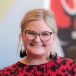 Woman with glasses and dangling earrings smiles.