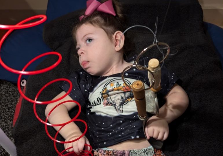 A child is in an adapted seat glancing at a red slinky from above.